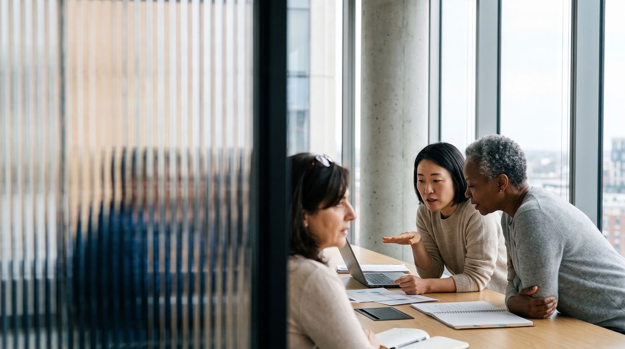 Three colleagues working together around a laptop at a shared desk