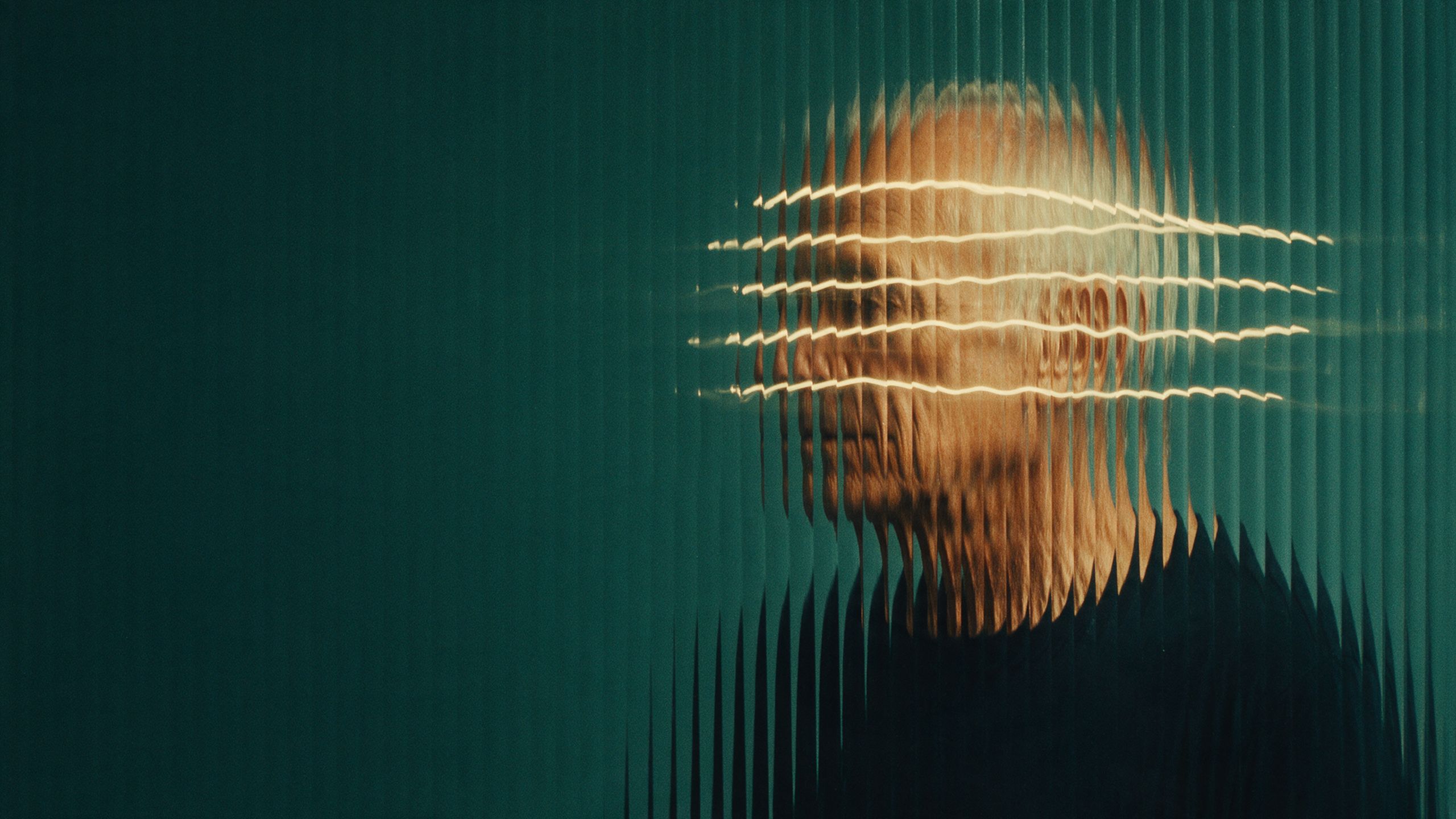 A portrait seen through ribbed glass, the face broken into vertical slices against a deep green background and crossed by bands of light